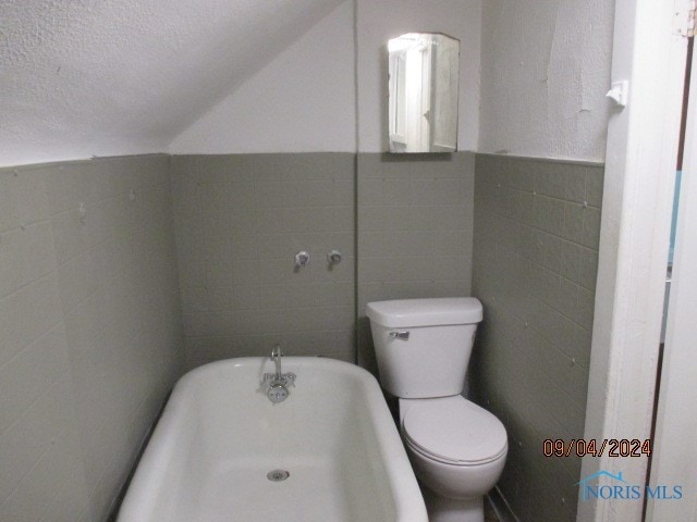 bathroom with tile walls, a textured ceiling, toilet, and a washtub