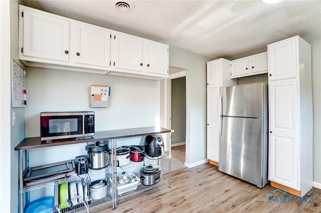 kitchen with white cabinets, a textured ceiling, appliances with stainless steel finishes, and light wood-type flooring