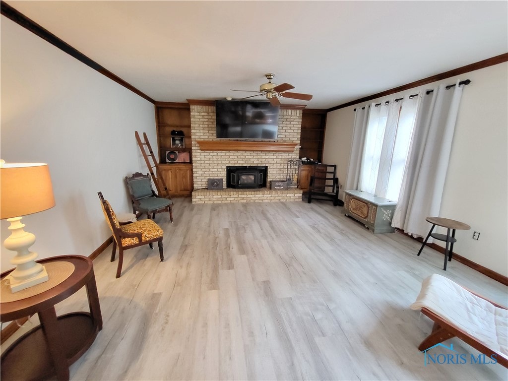 living room with ceiling fan, crown molding, light hardwood / wood-style floors, and a wood stove