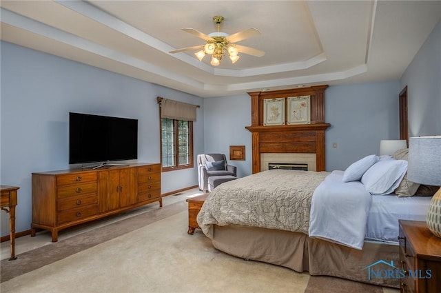 carpeted bedroom with a raised ceiling and ceiling fan