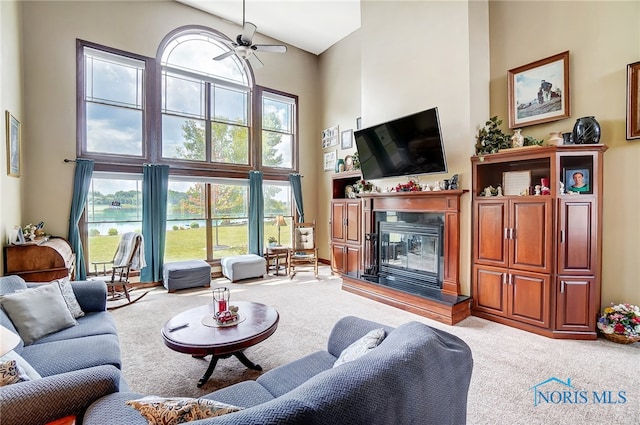 carpeted living room featuring ceiling fan and a towering ceiling