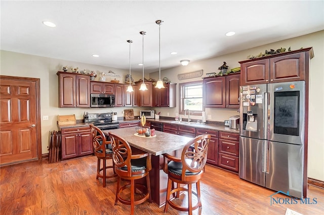 kitchen with decorative light fixtures, hardwood / wood-style floors, appliances with stainless steel finishes, a center island, and sink