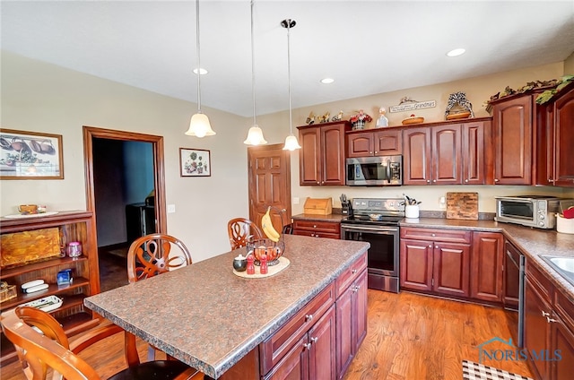 kitchen featuring a kitchen island, a kitchen breakfast bar, decorative light fixtures, light hardwood / wood-style flooring, and stainless steel appliances