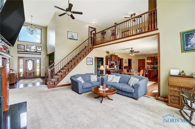 living room with ceiling fan with notable chandelier, a towering ceiling, a healthy amount of sunlight, and carpet floors