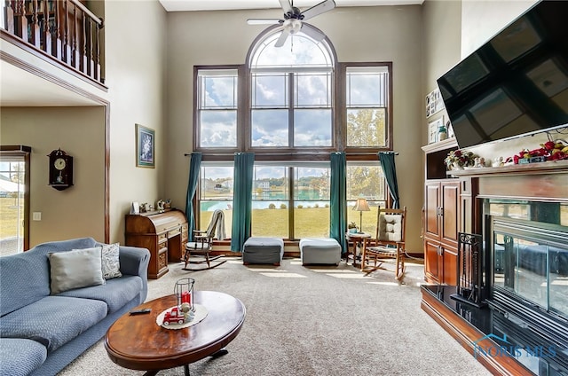 carpeted living room with ceiling fan and a high ceiling