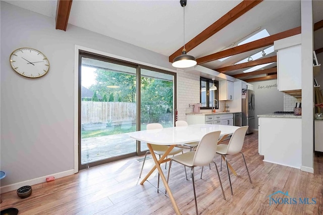 dining space featuring sink, vaulted ceiling with beams, and light hardwood / wood-style floors