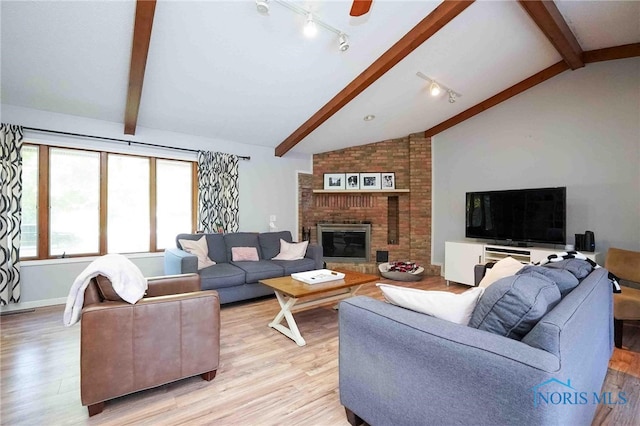 living room featuring light wood-type flooring, ceiling fan, a brick fireplace, and vaulted ceiling with beams