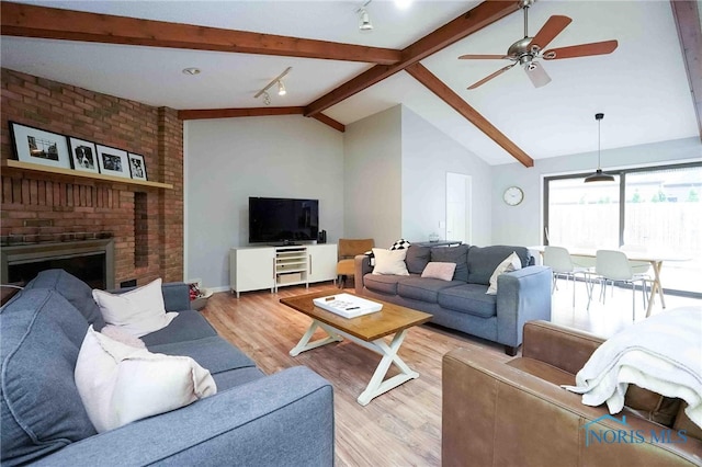 living room featuring light hardwood / wood-style flooring, ceiling fan, vaulted ceiling with beams, and a fireplace