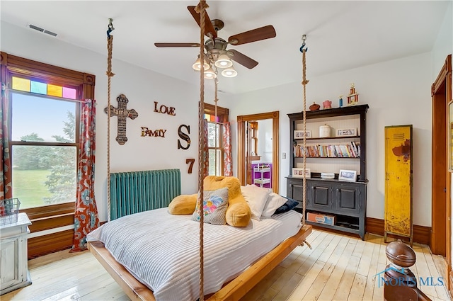 bedroom with multiple windows, light hardwood / wood-style floors, radiator, and ceiling fan