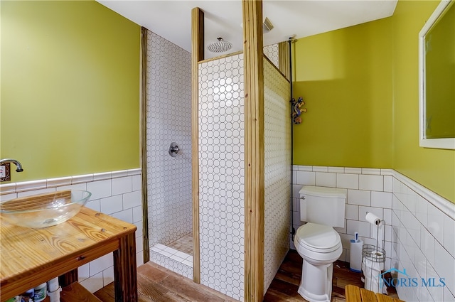 bathroom featuring tiled shower, hardwood / wood-style floors, toilet, and tile walls