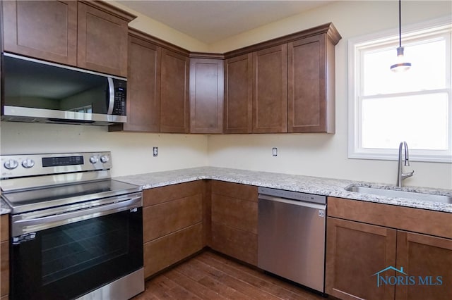 kitchen featuring decorative light fixtures, stainless steel appliances, light stone counters, sink, and dark hardwood / wood-style floors