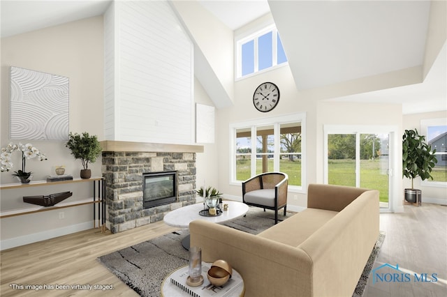 living room featuring light hardwood / wood-style floors, a stone fireplace, and high vaulted ceiling