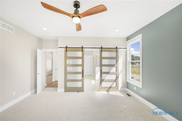 unfurnished bedroom featuring a barn door, light colored carpet, and ceiling fan