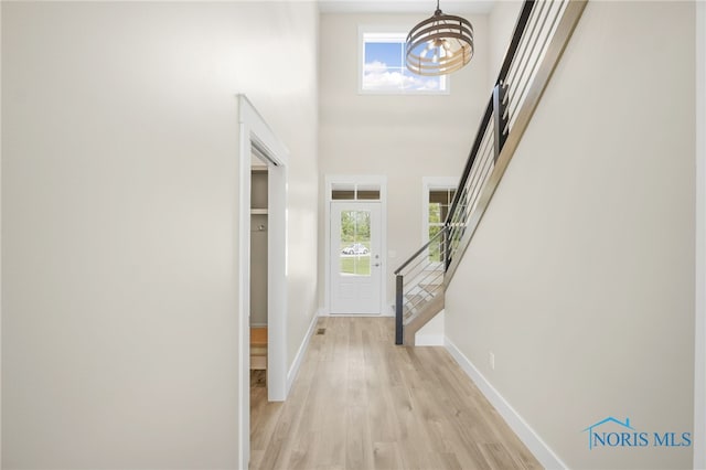 entrance foyer with a towering ceiling, light hardwood / wood-style flooring, and a notable chandelier