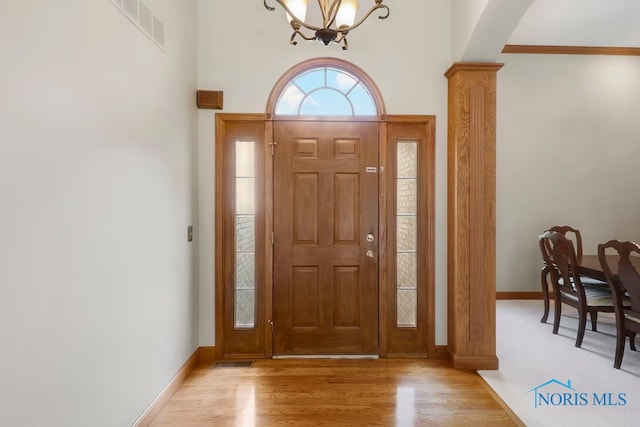 foyer entrance with light hardwood / wood-style flooring, a chandelier, and decorative columns