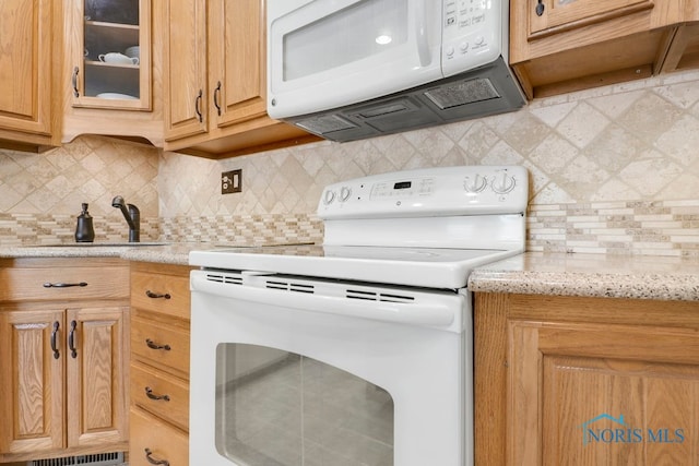 kitchen with backsplash, sink, light stone countertops, and white appliances