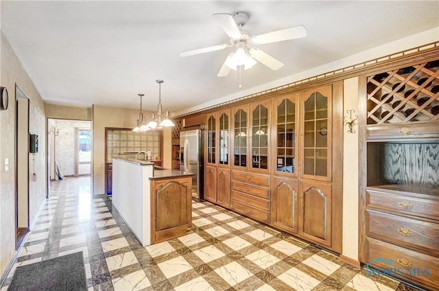 kitchen with hanging light fixtures, stainless steel fridge, ceiling fan with notable chandelier, and sink