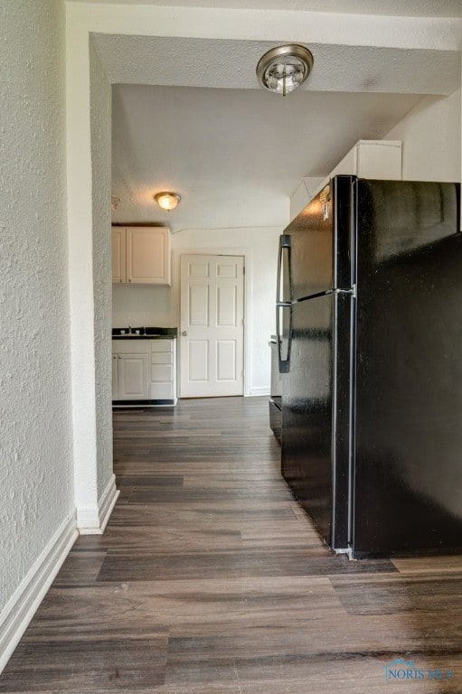 kitchen with white cabinetry, dark hardwood / wood-style floors, and black refrigerator