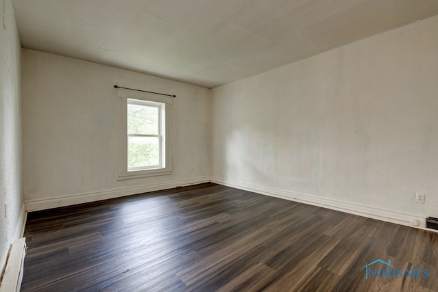 empty room with baseboard heating and dark hardwood / wood-style floors