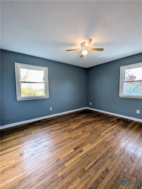 unfurnished room featuring a healthy amount of sunlight, dark wood-type flooring, and ceiling fan