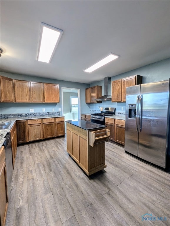 kitchen with a kitchen island, wall chimney range hood, light hardwood / wood-style flooring, stainless steel appliances, and sink