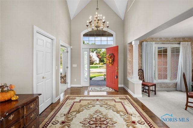 entrance foyer with dark wood-type flooring, an inviting chandelier, high vaulted ceiling, and decorative columns