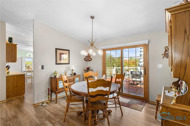 dining area featuring lofted ceiling, hardwood / wood-style floors, a chandelier, and a textured ceiling