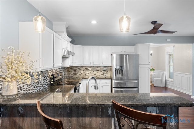 kitchen with dark stone counters, kitchen peninsula, hanging light fixtures, stainless steel appliances, and ceiling fan