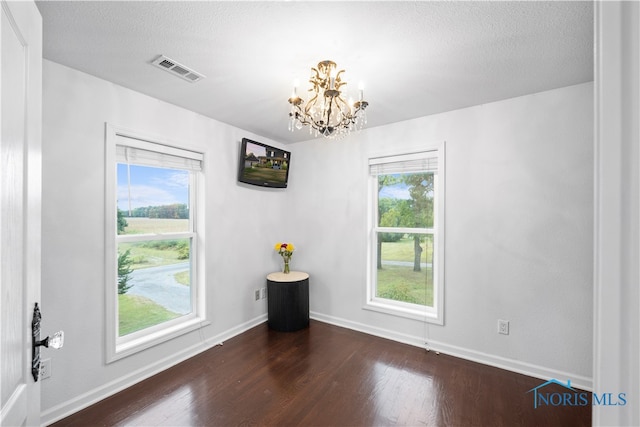 empty room featuring a textured ceiling, dark hardwood / wood-style floors, and a chandelier