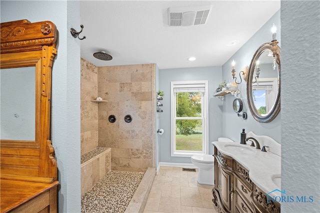 bathroom featuring tile patterned flooring, tiled shower, vanity, and toilet