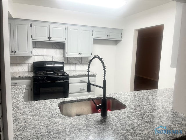 kitchen with light stone counters, black range, sink, and tasteful backsplash