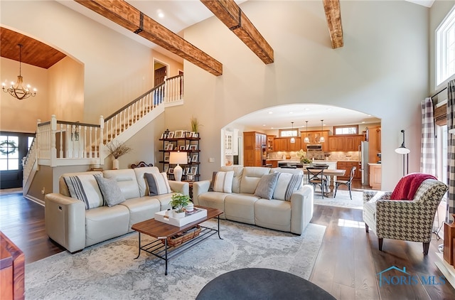 living room featuring a towering ceiling, beamed ceiling, a notable chandelier, and light hardwood / wood-style flooring