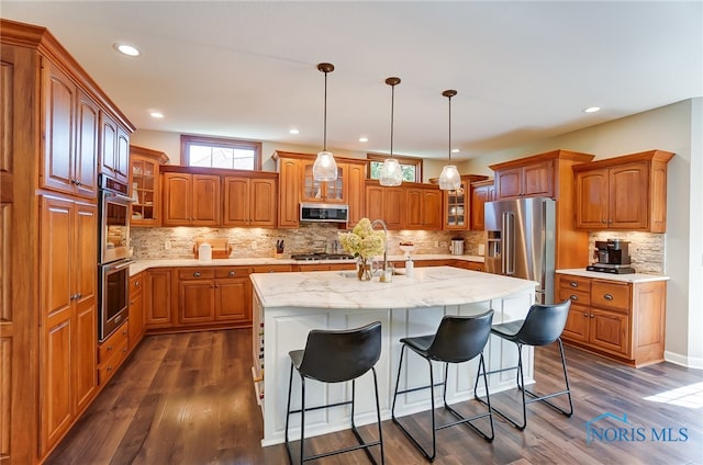 kitchen featuring an island with sink, stainless steel appliances, backsplash, and dark hardwood / wood-style flooring