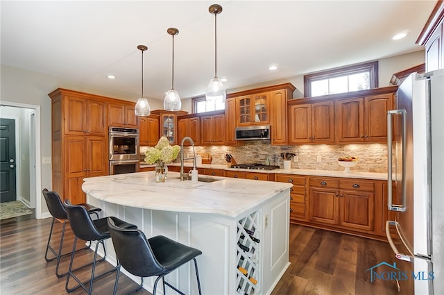 kitchen with a kitchen island with sink, decorative light fixtures, dark hardwood / wood-style flooring, sink, and appliances with stainless steel finishes