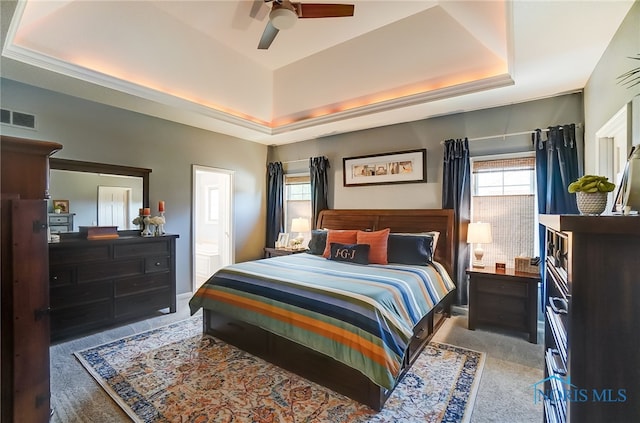 bedroom with carpet flooring, ceiling fan, a raised ceiling, and multiple windows