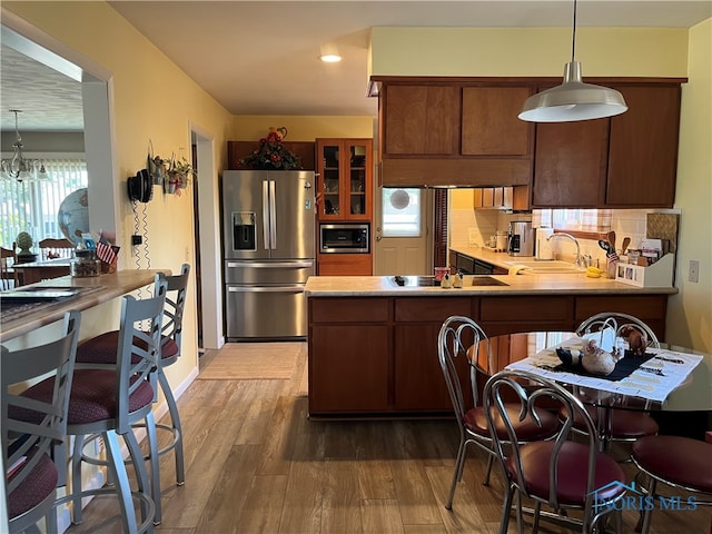 kitchen featuring hardwood / wood-style flooring, kitchen peninsula, appliances with stainless steel finishes, tasteful backsplash, and pendant lighting