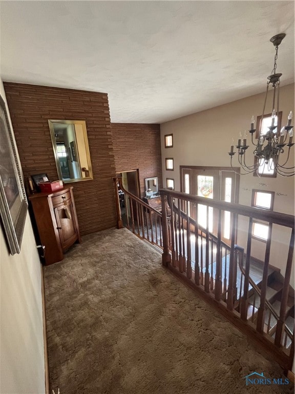 corridor featuring an inviting chandelier and dark colored carpet