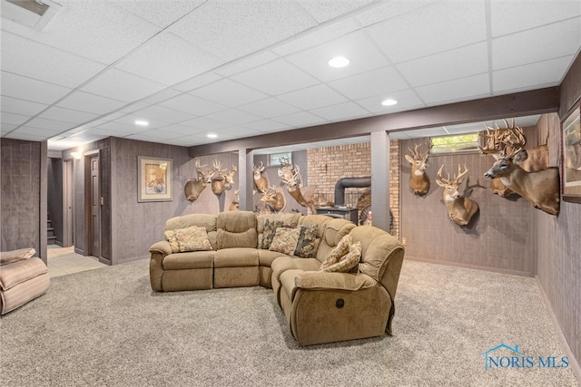 home theater room featuring a paneled ceiling, a wood stove, and light colored carpet