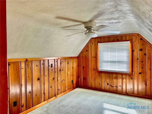 additional living space with a textured ceiling, lofted ceiling, wooden walls, and ceiling fan