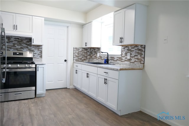 kitchen featuring sink, tasteful backsplash, white cabinetry, stainless steel stove, and light wood-type flooring