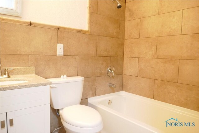 full bathroom with tile walls, tiled shower / bath, vanity, and toilet