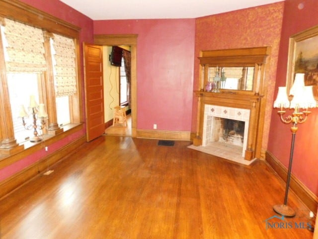 unfurnished living room featuring a tile fireplace, a wealth of natural light, and hardwood / wood-style flooring