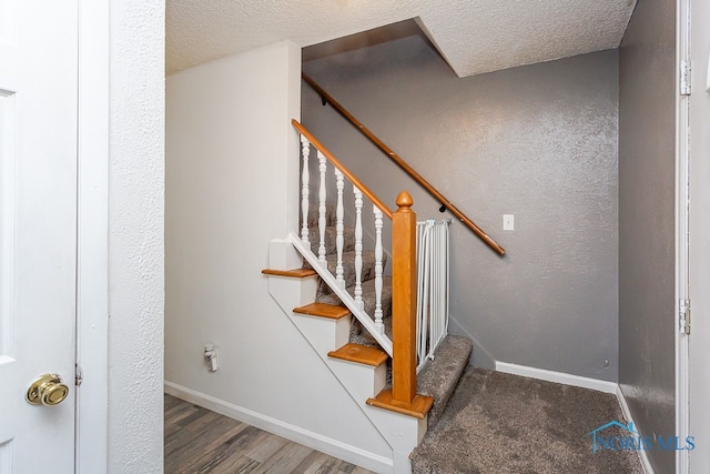 staircase with a textured ceiling and wood-type flooring