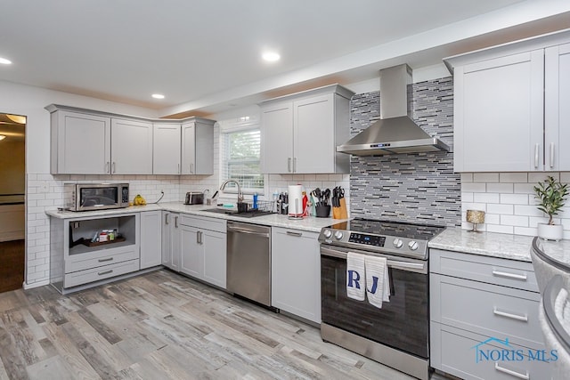 kitchen featuring tasteful backsplash, stainless steel appliances, light hardwood / wood-style flooring, sink, and wall chimney range hood