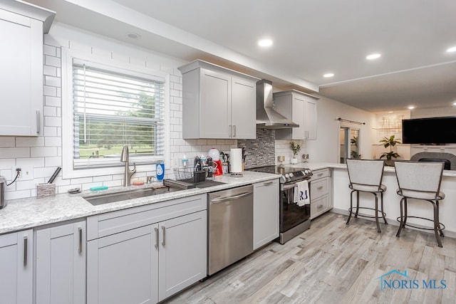 kitchen featuring sink, wall chimney exhaust hood, backsplash, light hardwood / wood-style flooring, and appliances with stainless steel finishes