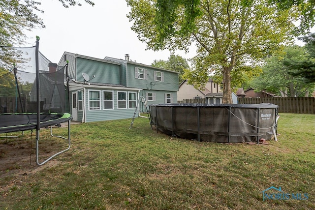 back of property with a yard, a fenced in pool, and a trampoline