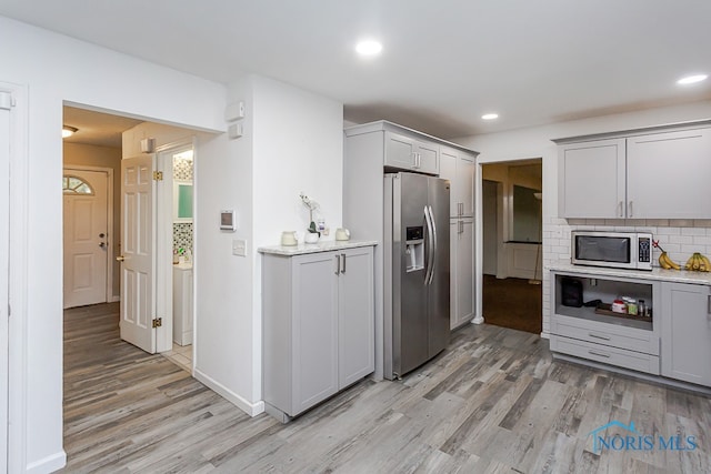 kitchen featuring gray cabinetry, light hardwood / wood-style floors, tasteful backsplash, light stone countertops, and stainless steel appliances