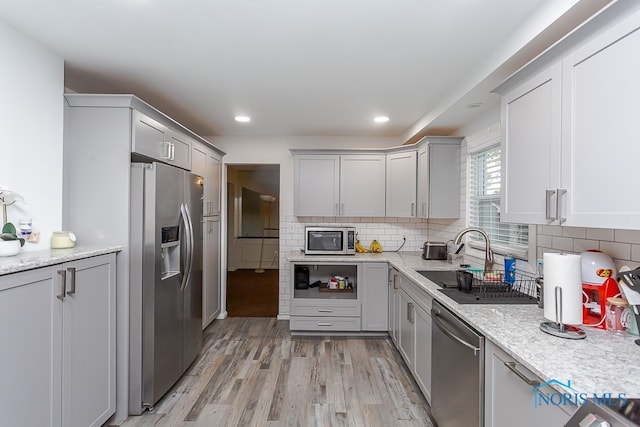 kitchen with light hardwood / wood-style floors, tasteful backsplash, sink, gray cabinetry, and stainless steel appliances