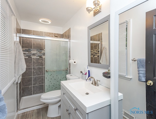 bathroom with wood-type flooring, vanity, toilet, and a shower with door