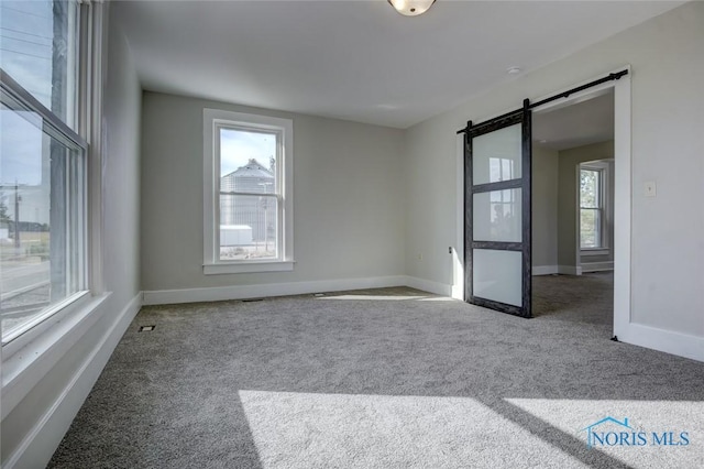 spare room with a barn door, baseboards, and carpet floors